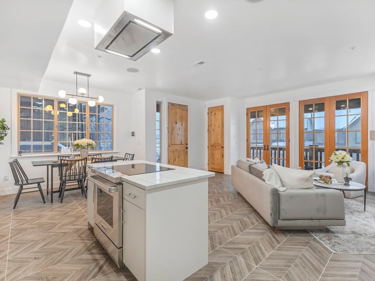 Modern open-concept kitchen and living room with white island, dining area, and sofa overlooking large windows