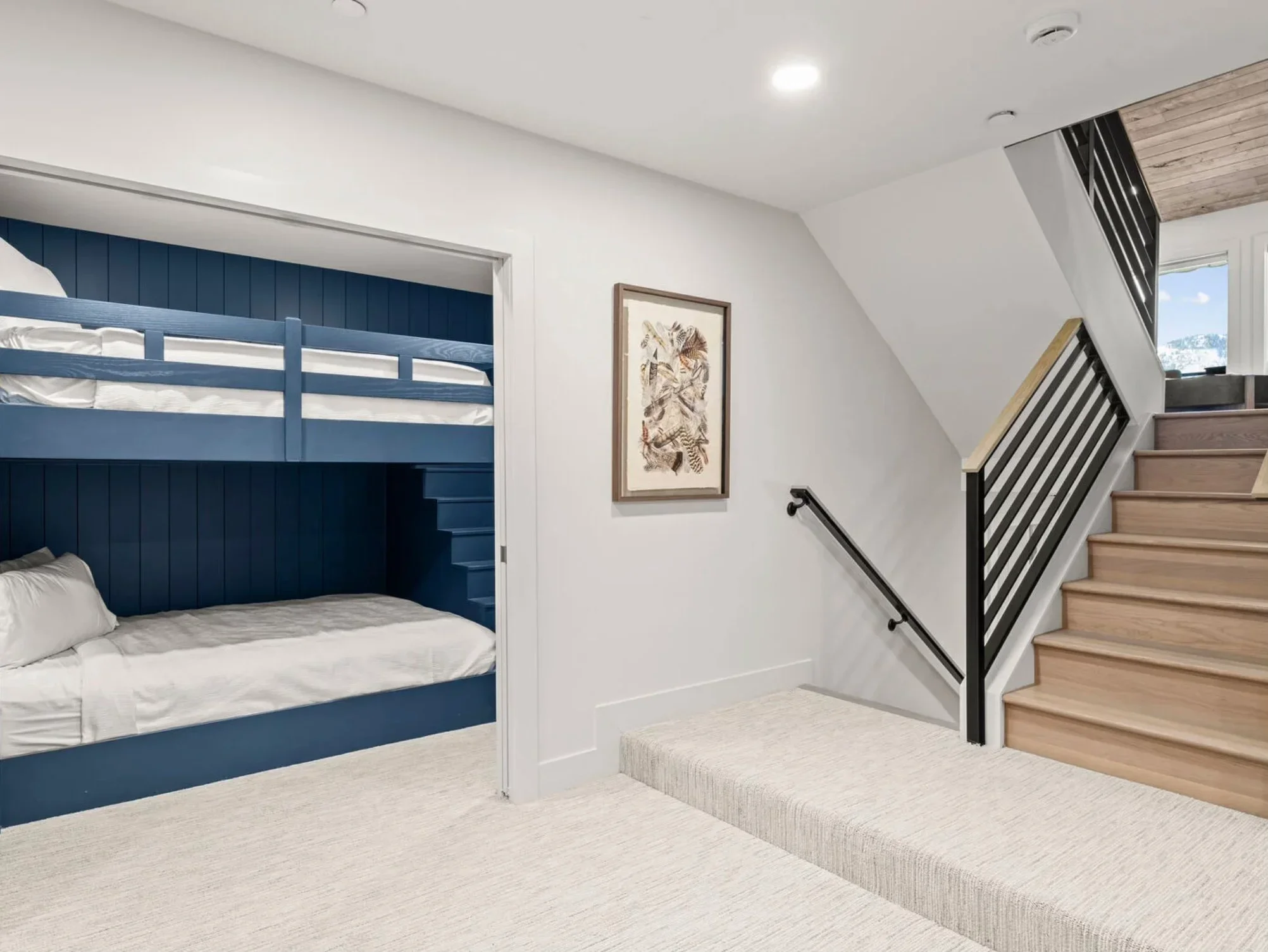 Loft bedroom with navy shiplap bunk beds, black metal railing, hardwood stairs, and white walls