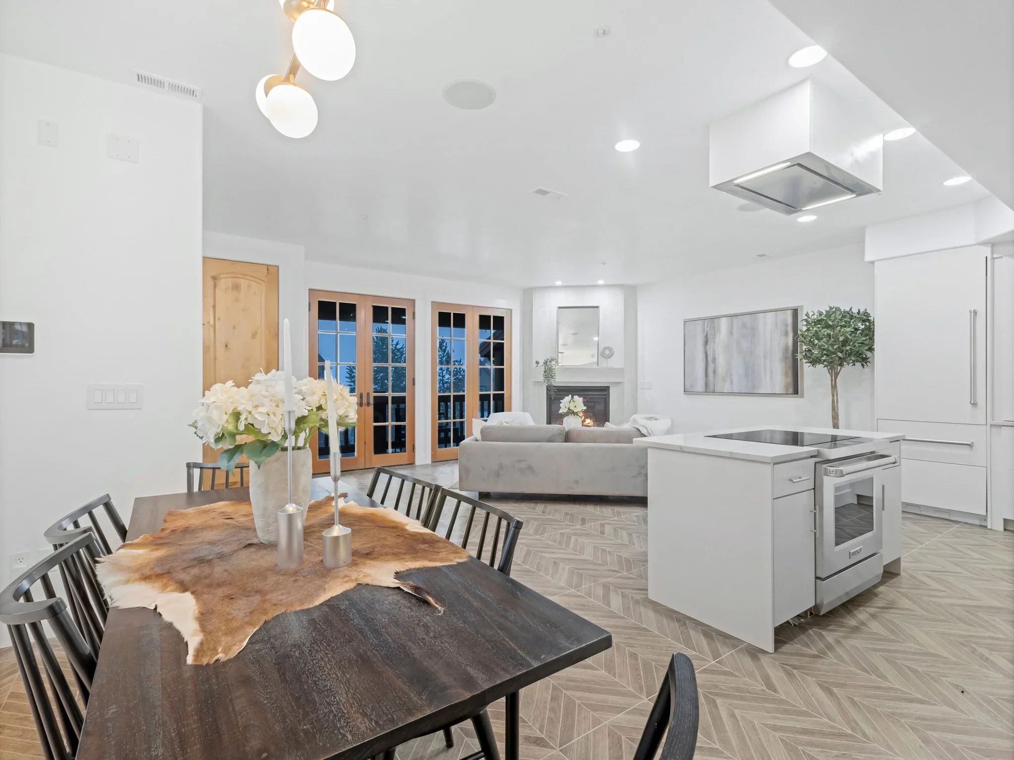 Modern kitchen with white cabinetry, stainless steel appliances, island, herringbone flooring, and open living area