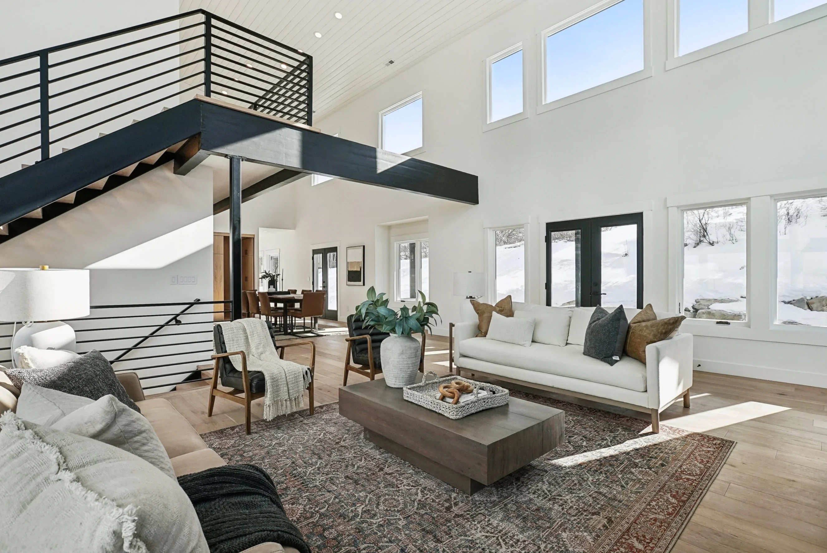 Modern living room with vaulted ceilings, steel mezzanine, hardwood floors, and black metal railings
