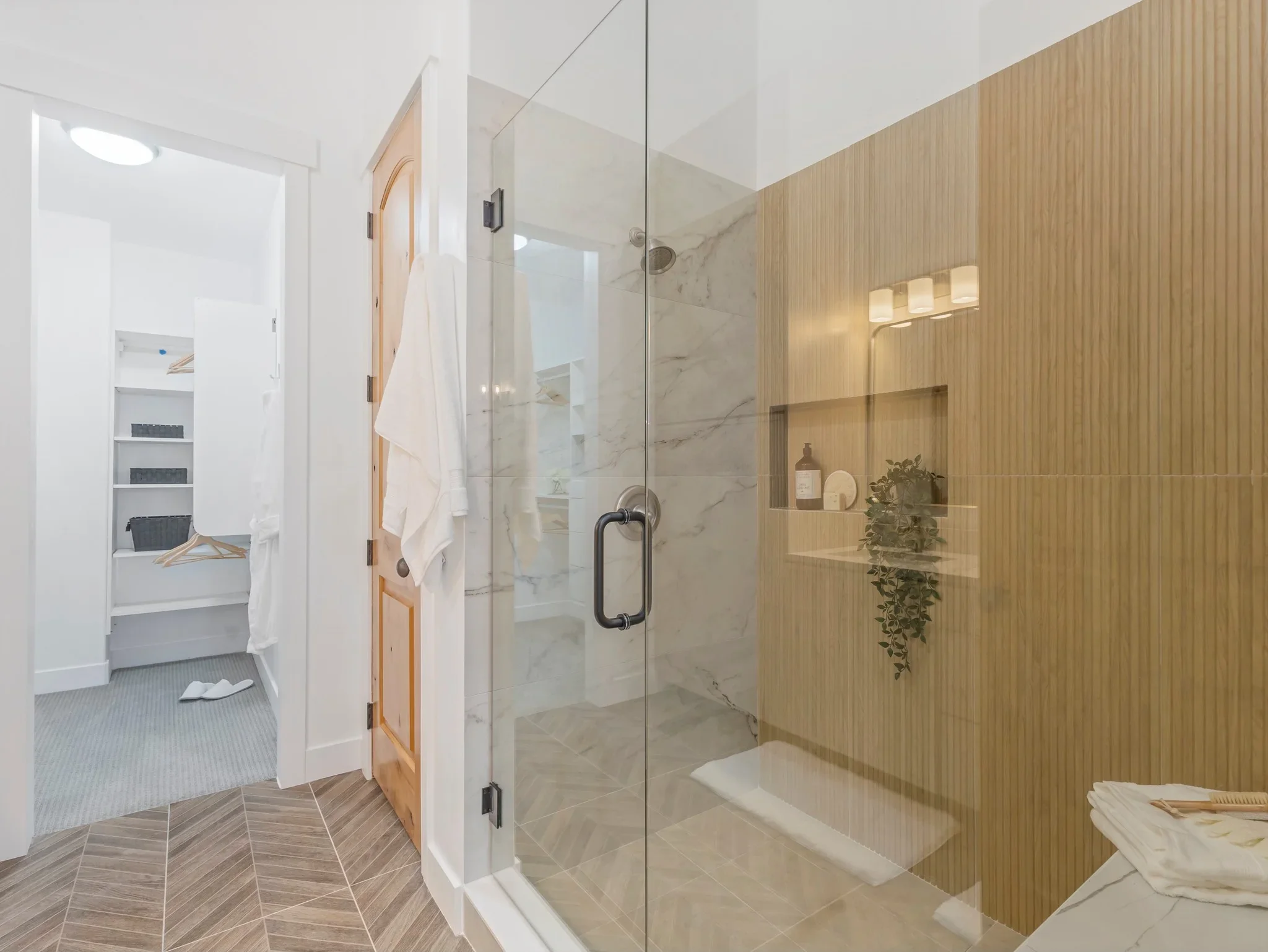 Modern bathroom with frameless glass shower, marble tile, wood accent wall, and herringbone flooring