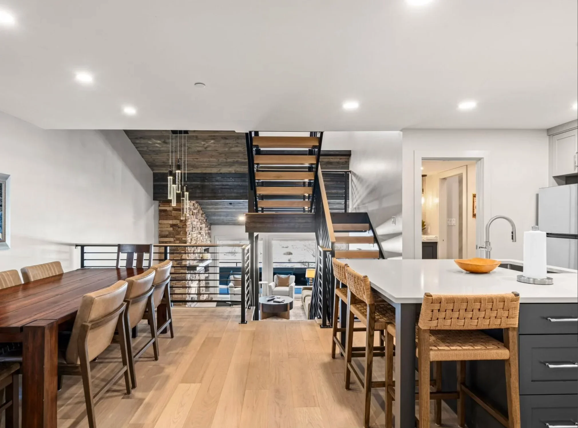 Modern kitchen with white quartz island, dark cabinetry, open staircase, and recessed lighting
